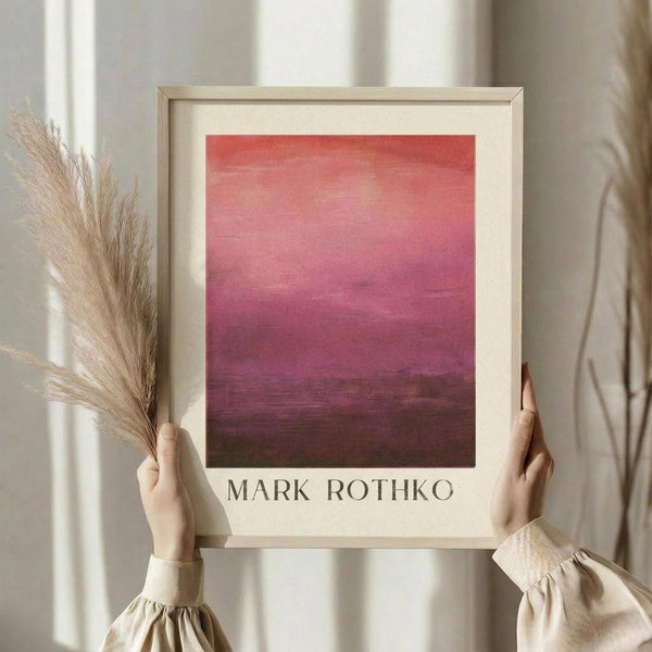 May include: Person in beige clothing with puffy sleeves holding a framed art print featuring a pink to burgundy gradient color field painting, with dried pampas grass in left hand, standing against white curtained window background in natural lighting