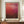May include: Framed art print featuring deep red and burgundy abstract color field painting with darker earth tones along bottom, displayed on wooden sideboard next to white ceramic vase and stacked books in elegant room with cream walls and white wainscoting