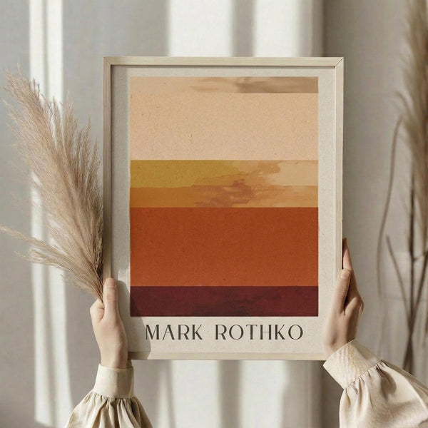 May include: Person holding framed abstract art print featuring horizontal bands of warm colors transitioning from cream at top through yellow, orange, to deep burgundy at bottom, displayed against white curtained window with dried pampas grass, in light wooden frame on white mat