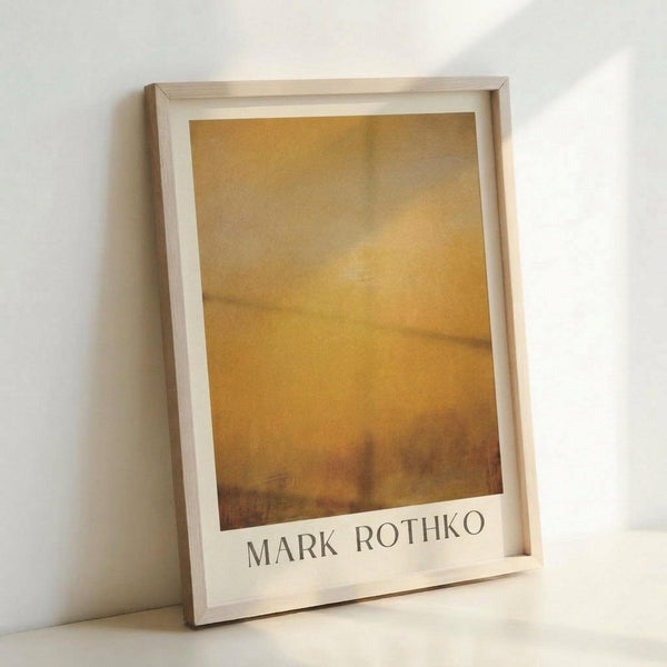 May include: Framed abstract painting print in warm golden and amber tones with soft, hazy brushstrokes creating a dreamy, atmospheric effect. The artwork features horizontal bands of color transitioning from lighter yellows at top to deeper oranges and browns at bottom. Displayed in a light wooden frame with white matting, leaning against a white wall in soft natural lighting.