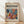 May include: Framed poster with cream background displaying abstract botanical artwork in vibrant blues, oranges, reds, and yellows. The colorful cut-out style design features flowing organic shapes and leaf-like forms. Bold black text reads "matisse" and "modernist" at top, with smaller text below the artwork. Natural wood frame leans against white wall on light wooden floor with soft window light creating shadows.