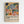 Colorful abstract botanical artwork in wooden frame hanging on white wall. Features vibrant painted leaves, flowers, and organic shapes in blues, greens, oranges, and pinks with yellow background. Below the artwork is white text reading "Celebrating Colors of Life" with descriptive paragraph about Matisse-inspired design. Modern minimalist room setting with clean presentation.