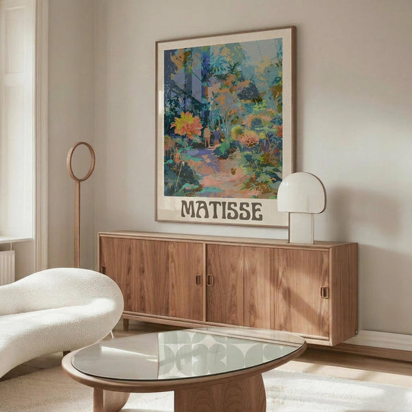 May include: Colorful botanical art print with "MATISSE" text displayed above wooden sideboard in modern living room. Vibrant tropical garden scene features blues, greens, oranges in painterly style. Thin wooden frame complements walnut furniture, white sculptural lamp, cream chair, and glass coffee table on neutral walls.