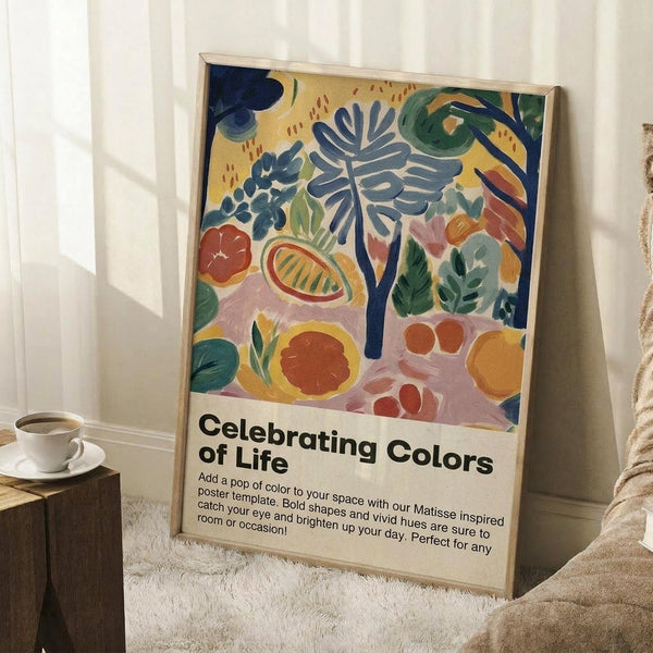 May include: Framed poster with colorful Matisse-style botanical illustration featuring tropical leaves, fruits, and abstract shapes in blues, greens, oranges, and pinks on cream background. White text below reads "Celebrating Colors of Life" with descriptive paragraph. Light wood frame leans against white wall corner next to coffee cup on wooden side table and cream knit throw blanket on white textured rug.