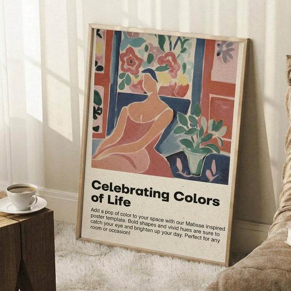 May include: Framed colorful abstract poster leaning against white wall beside cozy armchair and wooden side table with coffee cup. Artwork features stylized woman figure surrounded by vibrant flowers and foliage in Matisse-inspired cut-out style using coral, blue, green and pink tones. Bold text reads "Celebrating Colors of Life" with descriptive text below. Natural lighting creates soft shadows on textured rug.