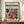 May include: Framed modernist art poster with abstract colorful leaf and floral shapes in blues, oranges, yellows, and pinks displayed on wooden sideboard beside white ceramic vase and stacked books against cream paneled wall