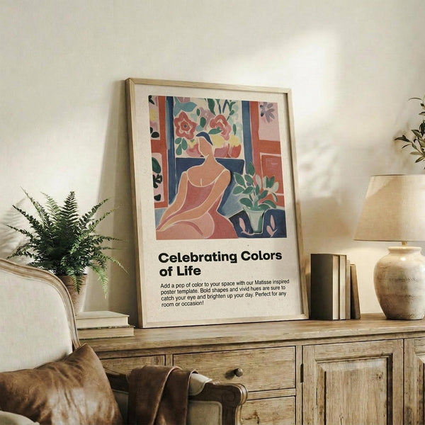 May include: Framed poster with Matisse-inspired artwork showing a seated woman in coral tones surrounded by colorful floral patterns and geometric shapes, displayed on a rustic wooden console table alongside books, a ceramic vase, and fern plant in a neutral-toned living room setting with beige chair and wall.