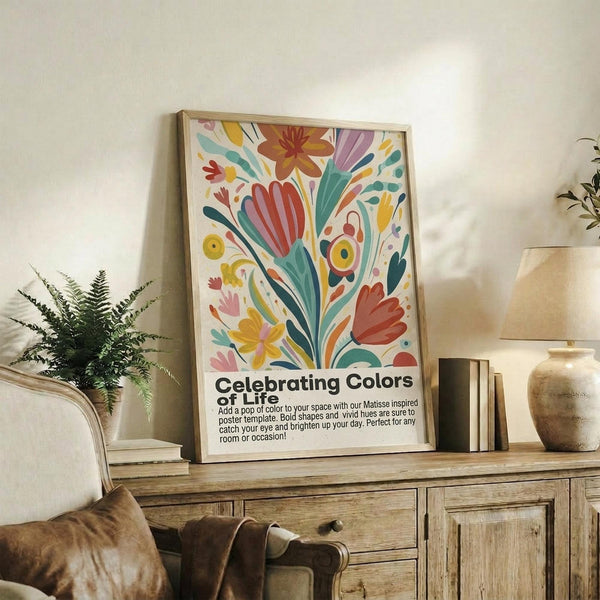 May include: Colorful abstract floral poster with vibrant red, yellow, teal and pink organic shapes in Matisse cut-out style, displayed in light wood frame on rustic wooden sideboard. Room setting shows cream upholstered chair, small potted fern, ceramic vases, and stacked books against white wall with warm natural lighting.