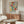 May include: Colorful Matisse-inspired floral poster with bold red, yellow, green, and orange abstract flowers and leaves, displayed above a mid-century modern walnut credenza in a bright living room with white curved chair, brass floor lamp, and glass coffee table on light wood floors