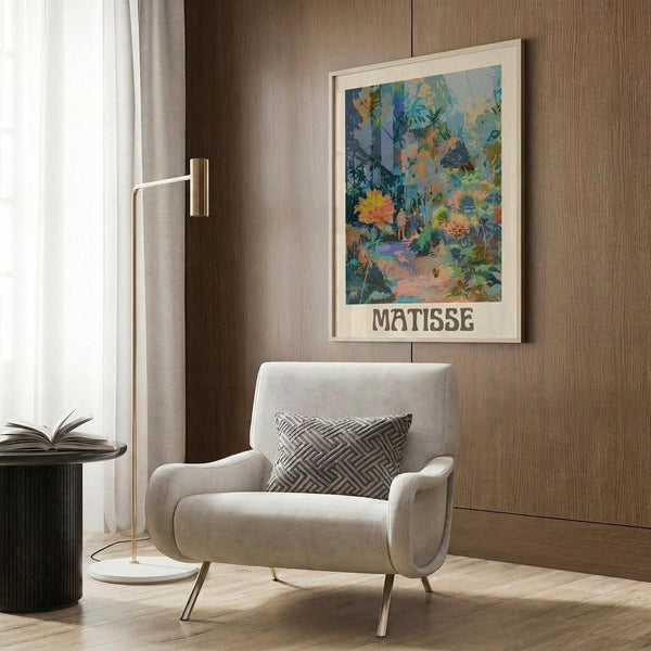 May include: Framed botanical art print with tropical garden scene in blues, greens, and coral colors, displayed on wood-paneled wall above beige upholstered armchair with geometric patterned pillow. Golden floor lamp and dark side table with open book visible in modern neutral-toned room setting.