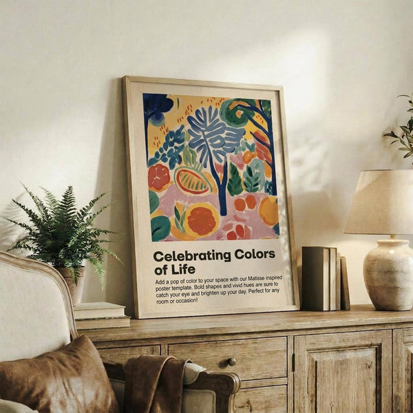 May include: Framed colorful botanical art print displayed on rustic wooden sideboard in modern living room. Artwork features vibrant abstract plants, fruits and leaves in blues, oranges, greens and pinks with "Celebrating Colors of Life" text below. Scene includes fern plant, ceramic vases, books, cream upholstered chair and neutral walls with natural lighting.