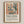 May include: Framed art print in natural wood frame mounted on cream wall. The artwork features a colorful interior scene with window, vase of flowers, and fruit bowl in muted earth tones of terracotta, sage green, and cream. Below the illustration is black text reading "Matisse: A Master of Color and Form" followed by descriptive paragraph about Henri Matisse exhibition.