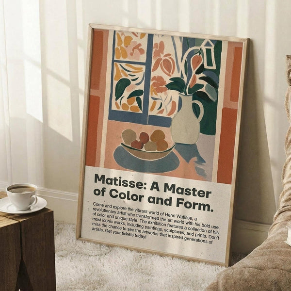May include: Framed art poster leaning against white wall on wooden floor next to coffee cup and saucer. Artwork shows colorful interior scene with window, vase of flowers, and fruit bowl in warm earth tones of orange, green, and cream. Exhibition-style poster includes descriptive text below the artwork. Natural lighting creates soft shadows across the cozy room setting with textured rug visible.