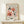 May include: Framed vintage-style art print featuring abstract cut-out shapes in coral pink, terracotta, and black against cream background, displayed on light wood console table with small wrapped gift box beside it on white wall