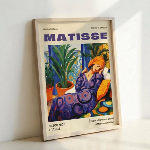 May include: Framed museum exhibition poster featuring a colorful Matisse-style illustration of a woman in purple patterned clothing with an orange head wrap, sitting among potted plants. The poster has purple "MATISSE" text at top and "06200 NICE, FRANCE" at bottom. Light wood frame leans against white wall, showing vibrant blues, oranges, and greens in the artwork.
