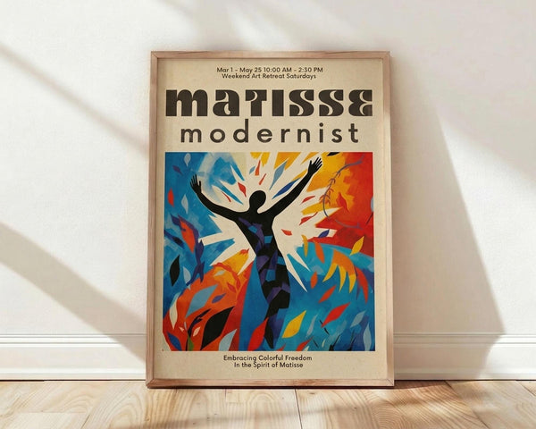 May include: A framed art poster leaning against a white wall on light wood flooring. The poster features a stylized black silhouette of a person with arms raised, surrounded by vibrant blue, orange, red and yellow abstract foliage shapes in a Matisse-inspired cut-out style. The design has a cream background with bold typography reading "matisse modernist" at the top and event details. Natural light creates soft shadows on the white fabric backdrop.