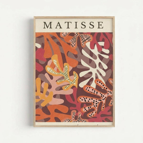 Framed art print featuring abstract cut-out shapes in warm tones of orange, coral, burgundy, yellow and cream. The composition shows organic, flowing forms with various patterns including crosshatch and polka dots. Some shapes resemble coral or seaweed with flowing tendrils. The artwork has "MATISSE" printed at the top in black letters on cream background. Natural wood frame hangs on white wall.