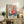 May include: Colorful floral art print with vibrant pink, orange, and blue flowers in Matisse's distinctive style, displayed in light wood frame on rustic wooden sideboard alongside fern plant, ceramic vase, and stacked books in cozy living room setting with cream upholstered furniture and warm natural lighting.