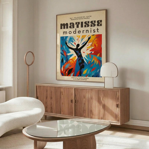 May include: Colorful modernist poster featuring a silhouetted figure with raised arms surrounded by vibrant blue, orange, and red abstract shapes, displayed in a thin wooden frame above a walnut credenza. Scene shows minimalist living room with white curved chair, glass oval coffee table, and warm natural lighting creating soft shadows on cream walls.
