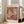 May include: A framed art print leaning against a white wall beside a beige upholstered sofa. The poster features abstract cut-out shapes in warm tones of orange, burgundy, yellow, and cream with cross-hatched patterns and organic coral-like forms. White text reads "MATISSE" at top and "PAPIERS DÉCOUPÉS" at bottom. Natural sunlight streams through tall windows onto hardwood floors in this minimalist living room setting.