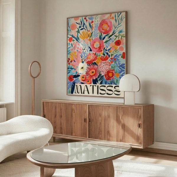 May include: Colorful floral art print with vibrant pink, orange, and blue flowers in an abstract style, displayed in a thin frame above a walnut wood credenza. Modern living room setting features a white curved chair, glass-top oval coffee table, and warm neutral walls with natural lighting.
