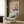 May include: Modern living room with beige armchair and geometric pillow, brass floor lamp, dark side table with open book, and framed floral art print on wood-paneled wall. The colorful botanical artwork features vibrant pink, coral, blue and yellow flowers in an abstract style with "MATISSE" text below the bouquet design.