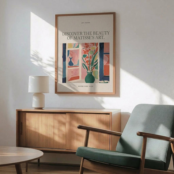 May include: Framed art poster featuring colorful abstract interior scene with green vase of flowers, geometric shapes in coral, blue, and pink tones. Displayed above mid-century modern wooden credenza with white ceramic lamp. Sage green upholstered chair with wooden arms positioned nearby. Natural sunlight creates soft shadows on white wall.