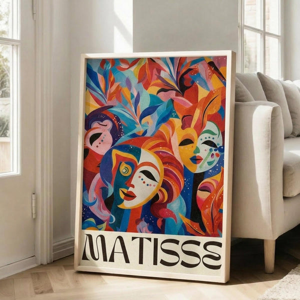 May include: Large framed poster with vibrant abstract artwork featuring colorful stylized faces and masks surrounded by flowing foliage in blues, oranges, reds, and yellows. The word "MATISSE" appears in bold black letters at the bottom. The poster leans against a white wall next to a beige sofa in a bright, minimalist living room with large windows and natural lighting.