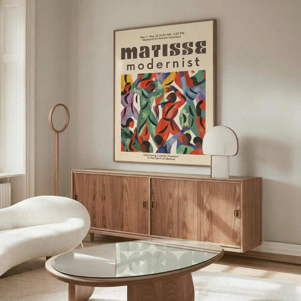 May include: Colorful Matisse modernist exhibition poster with abstract cut-out shapes in red, green, blue, and purple displayed above a mid-century walnut credenza. Modern living room setting features white sculptural chair, glass oval coffee table, and warm natural lighting creating shadows on neutral walls.