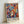 May include: Framed poster print leaning against white wall showing vibrant abstract artwork with stylized faces and foliage in bold colors including blues, reds, oranges, and yellows. The composition features mask-like faces with decorative patterns surrounded by flowing leaf motifs. Text reading "MATISSE" appears at bottom in black letters. Natural wood frame visible around edges.