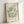 May include: Framed art print leaning against white wall showing green coral-like cutout shapes on cream background with "MATISSE" text at top and "BERGGRUEN & CIE" gallery information at bottom. Light wood frame with natural lighting creating soft shadows on the wall.