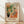 May include: Framed art print in light wood frame leaning against white wall on wooden floor. Colorful interior scene showing orange upholstered chair with leopard print pillows, black vase with tropical plants and orange flowers, patterned floor tiles, and window view. Warm palette of oranges, greens, and earth tones in decorative flat style with "MATISSE" text below image.
