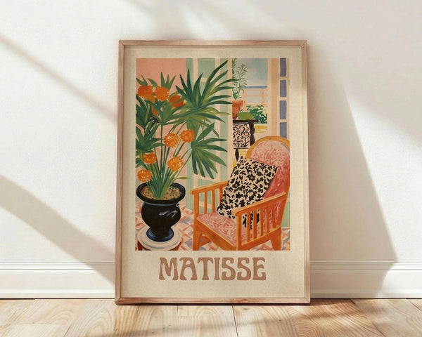 May include: Framed art print in light wood frame leaning against white wall on wooden floor. Colorful interior scene showing orange upholstered chair with leopard print pillows, black vase with tropical plants and orange flowers, patterned floor tiles, and window view. Warm palette of oranges, greens, and earth tones in decorative flat style with "MATISSE" text below image.