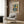 May include: Framed Matisse art poster featuring abstract blue figure in cut-out style with colorful geometric shapes in red, yellow, and orange. White matted frame hangs on wood panel wall above beige upholstered armchair with geometric patterned pillow. Modern reading corner with brass floor lamp and dark side table.