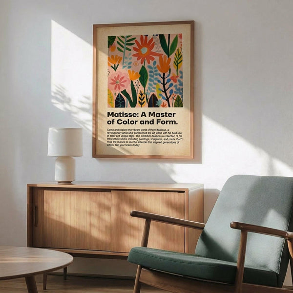 May include: Framed botanical art print with colorful flowers and leaves in Matisse-inspired style, displayed above wooden sideboard with ceramic lamp. Mid-century modern living room setting features sage green upholstered armchair with wooden frame and round coffee table. Natural sunlight creates shadows on white wall. Print shows vibrant orange, pink, and green botanical motifs with descriptive text below artwork.