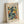 Framed art poster featuring an abstract blue figure in Matisse's cut-out style, with curved organic shapes in teal, navy, yellow and orange against a cream background. The wooden frame sits propped against a white wall, showing the poster's vertical rectangular format with "MATISSE" and "ART POSTER" text.