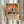 May include: Hands holding a framed poster featuring colorful botanical artwork with vibrant flowers and leaves in orange, pink, green, and blue against a peachy background. Below the artwork is text about a Matisse exhibition. The wooden frame is displayed against white curtains with dried pampas grass visible to the left. The person wears a cream-colored blouse with ruffled sleeves.