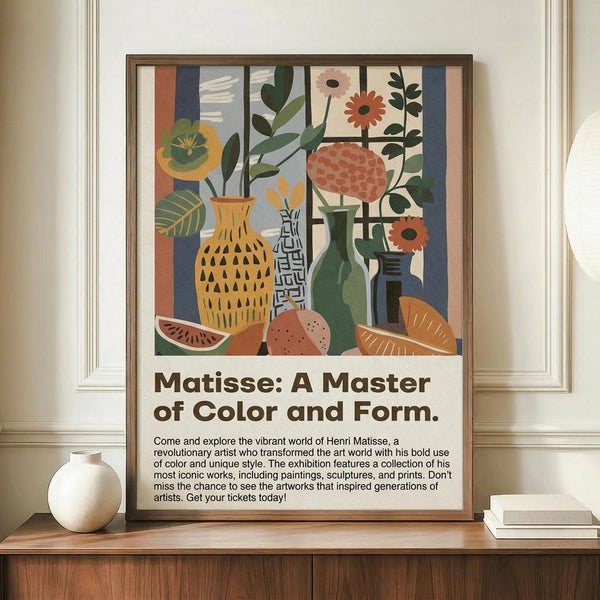 May include: Framed exhibition poster featuring colorful still life artwork with vases, flowers, and fruit in Matisse-inspired style, displayed on wooden sideboard next to white ceramic vase and books against cream wainscoted wall. Poster shows vibrant yellows, greens, oranges, and blues with bold geometric shapes and floral motifs. Brown wooden frame complements warm interior setting.