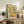 May include: Framed art poster with colorful fruit and botanical illustration in Matisse-inspired style, featuring yellow lemons, pink grapefruit, green leaves, and bottles on cream background. Displayed on rustic wooden sideboard with fern plant, books, ceramic vase, and brown leather chair in warm-toned living room setting.