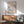 a living room with a framed poster of a colorful abstract painting hanging on the wall above a wooden cabinet. The cabinet has a white lamp on top of it. In front of the cabinet, there is a green armchair. The room has a wooden floor and a round wooden table.