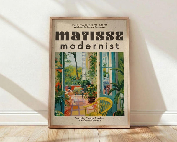May include: Framed art poster featuring a colorful indoor scene with tropical plants, yellow chair, and bright interior space in Matisse's distinctive style. The cream-colored poster displays "matisse modernist" text at top and "Embracing Colorful Freedom In The Spirit of Matisse" at bottom. Natural wood frame leans against white wall on light wooden floor with soft shadows.