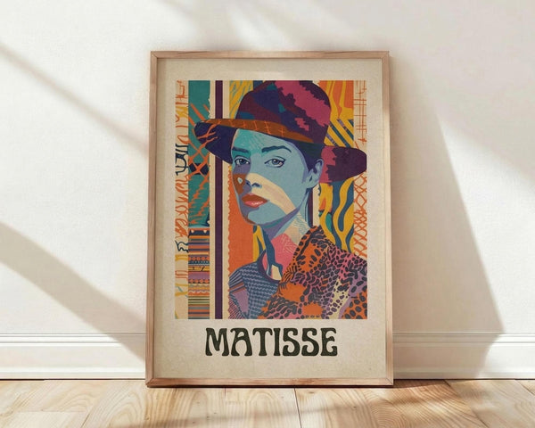 May include: Framed poster print featuring a vibrant portrait of a woman wearing a decorative hat, rendered in bold geometric patterns with teal, orange, purple, and yellow colors. The artwork combines modernist style with intricate textile-like designs and includes "MATISSE" text at bottom. Light wood frame sits against white wall on natural wood flooring with soft natural lighting creating diagonal shadows.
