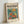 May include: Framed poster with cream mat featuring colorful Matisse-style artwork of orange goldfish in glass fishbowl with vibrant flowers - yellow, orange, and pink blooms against turquoise background. Bold "matisse modernist" typography at top with exhibition details. Natural wood frame leaning against white wall in bright lighting.