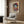 May include: Colorful Matisse-inspired art print of woman in decorative hat displayed in modern living room with beige armchair, geometric pillow, brass floor lamp, and dark wood paneled wall. Poster shows vibrant blues, purples, oranges in artistic portrait style with ornate patterned background elements.