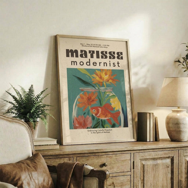 May include: Framed poster with cream matting displaying colorful modernist artwork of orange goldfish swimming among vibrant flowers in glass vase against teal background. Print sits on rustic wooden sideboard beside fern plant, ceramic vases, and books in warmly lit living room with beige sofa and neutral decor.