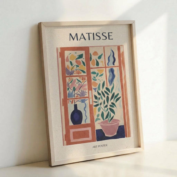 May include: Framed art poster in light wood frame leaning against white wall. Print features Matisse-style cut-out artwork depicting colorful window scene with geometric panels, plant motifs in green, blue, orange and pink tones, dark blue vase, and potted plant. Text reads "MATISSE" at top and "ART POSTER" at bottom on cream background.