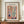 May include: Framed Matisse-style art poster displaying colorful cut-out inspired window scene with plants, blue vase, and botanical elements in warm terracotta tones. Wooden frame sits on walnut credenza beside white ceramic vase and stacked books against cream wainscoted wall.