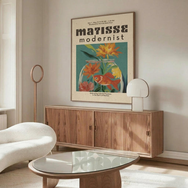 May include: Matisse-inspired modernist poster displayed above wooden sideboard in bright living room. Artwork features colorful goldfish in glass bowl with orange and yellow flowers against teal background. White upholstered chair and glass coffee table visible. Natural wood furniture with mid-century design. Soft natural lighting creates warm, contemporary interior styling.
