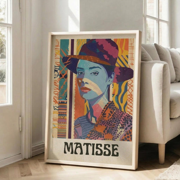May include: Framed colorful portrait poster of a woman wearing a hat, displayed in bright living room setting next to beige sectional sofa. Artwork features vibrant blues, oranges, yellows and geometric patterns in modernist style with "MATISSE" text at bottom. Natural wood frame, hardwood floors, white walls with large windows showing daylight.