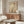 May include: Framed minimalist desert landscape artwork with warm earth tones, featuring a bare tree, rolling hills, pale yellow sun and small orange circle against beige background. Displayed above mid-century walnut credenza in modern living room with white curved chair, glass oval coffee table, and mushroom-style table lamp.